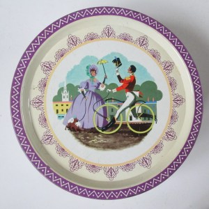 The Qualioty Street Soldier, ridimng a boneshaker bicycle, greets the Lady